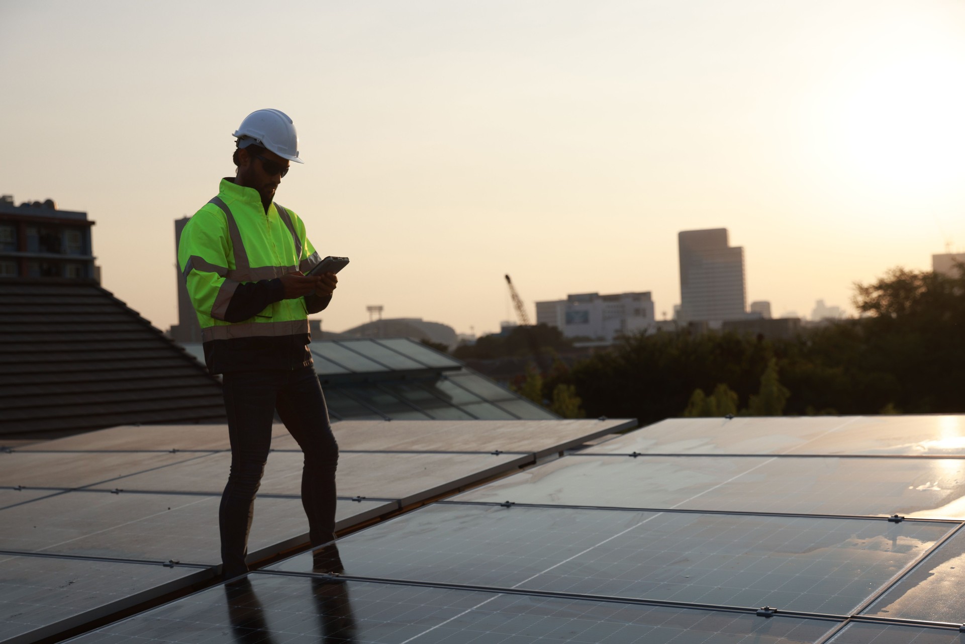 smart site solar engineer with a green safety jacket working on a solar rooftop, Specialist technician professional engineer with laptop and tablet maintenance checking to install solar roof panel on the factory rooftop under sunlight.